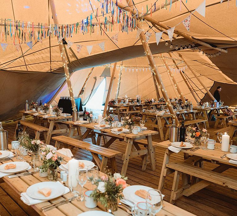 Inside the wedding tipi with wooden benches and handmade streamer decorations 