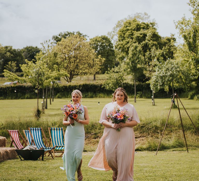 Bridesmaids in mismatched pastel bridesmaid dresses carry colourful floral bouquets 