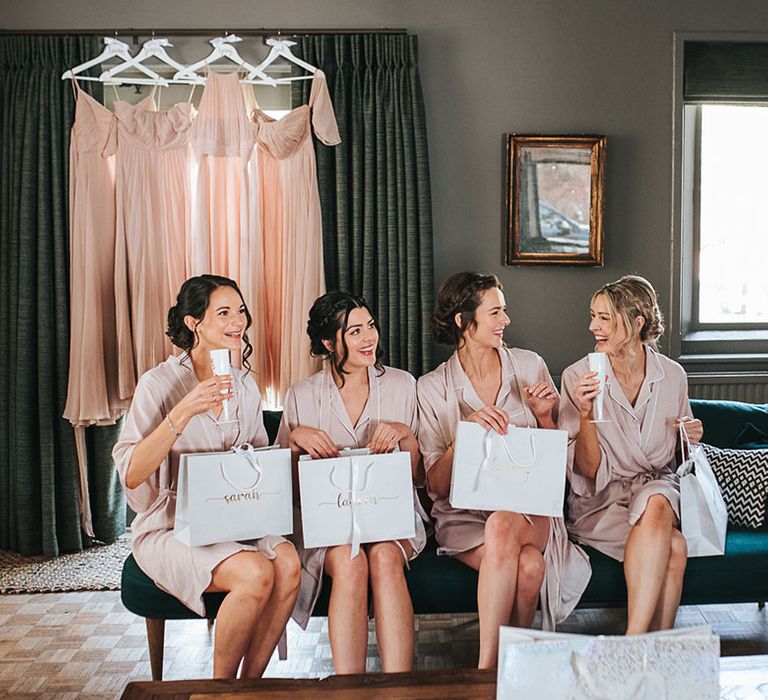 Bridesmaids all sit together in pink robes opening gifts on the morning of the wedding 