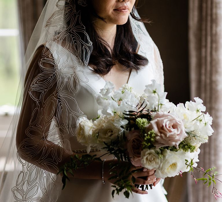 Bride wears her dark hair in loose curls and Princess wedding dress whilst holding small bridal bouquet 