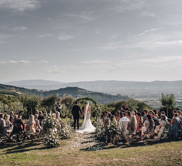 Bride & groom marry at Castello di Petrata Umbria Villa wedding outdoors complete with floral arch and beautiful mountain scenery 