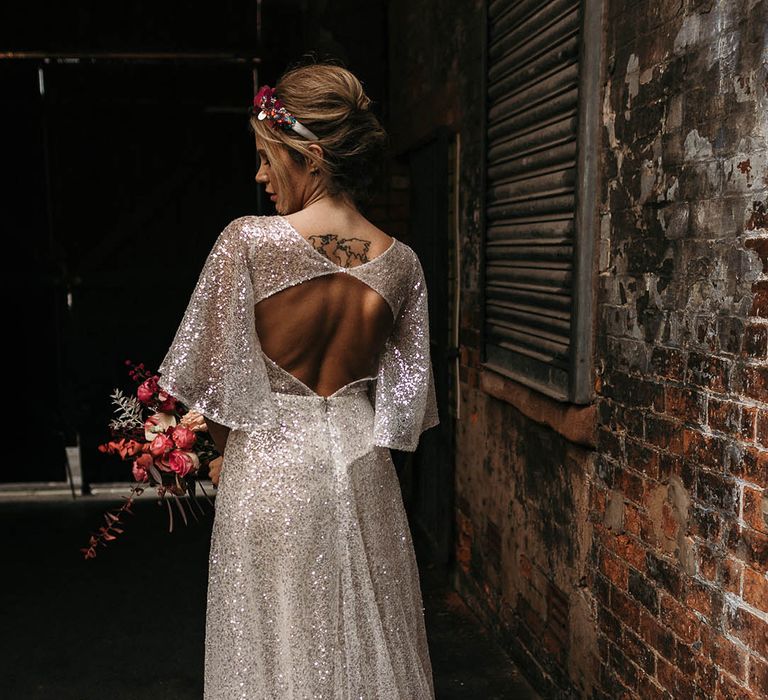 Bride wears open back batwing wedding dress with sparkling fabric whilst carrying colourful floral bouquet