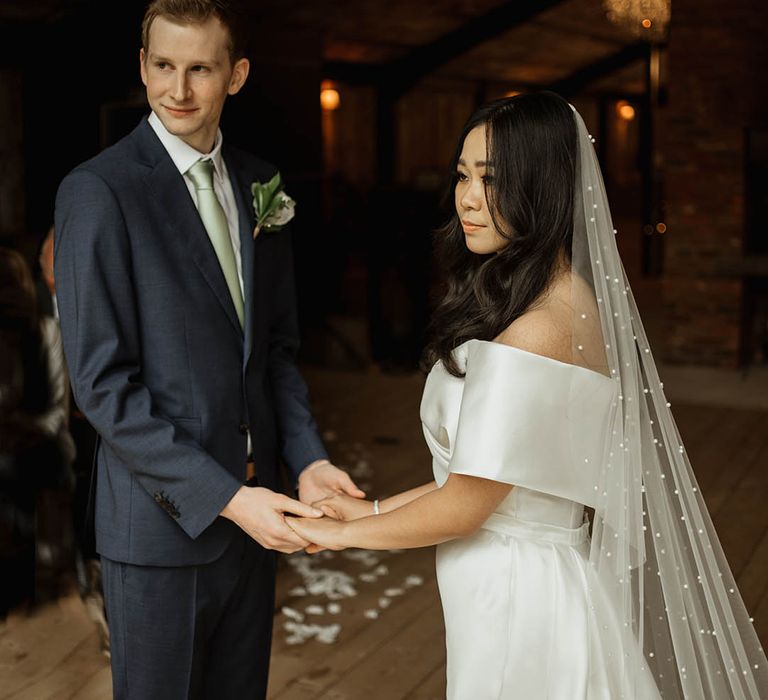 Elegant chic rustic luxe wedding with the bride in an off the shoulder wedding dress and pearl veil and groom in navy suit with sage green tie 