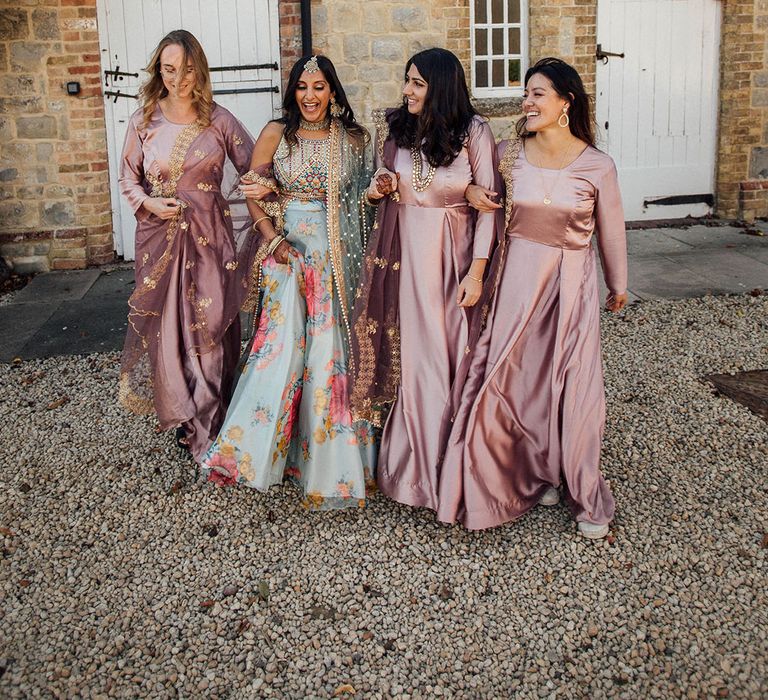 Bride stands besides her bridesmaids in long sleeve pink satin bridesmaid dresses with gold embellishment 