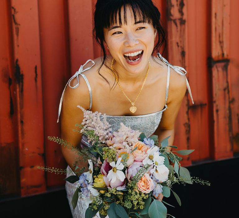 East Asian bride wears silver The Vampire's Wife wedding dress and holds homemade pastel bouquet 