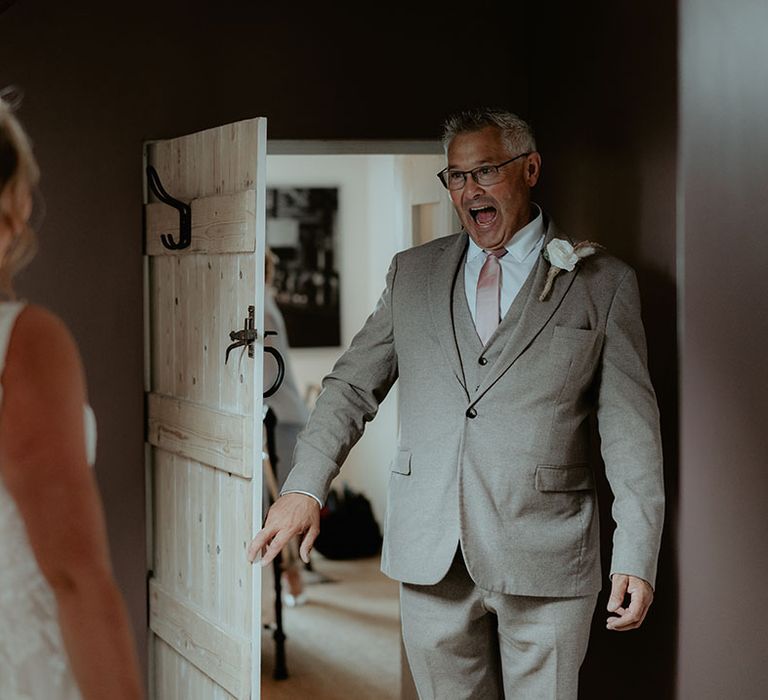 Brides father wearing grey three piece suit sees her for the first time on the morning of her wedding day