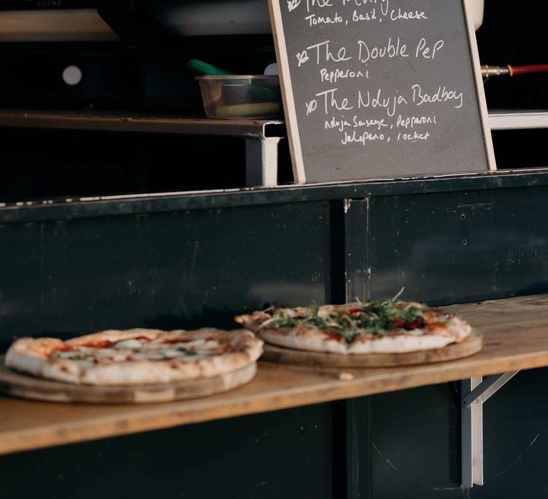 Wedding food ideas - mobile pizzeria with pizza ovens, a chalkboard menu and two freshly baked pizzas on the side 