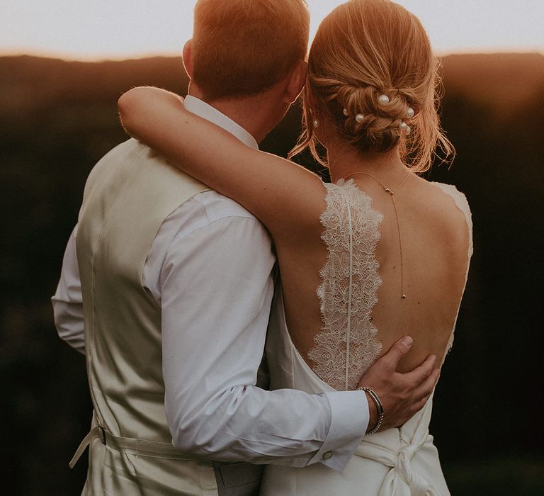 Bride in scallop lace detailed dress wraps her arm around her groom during golden hour portraits