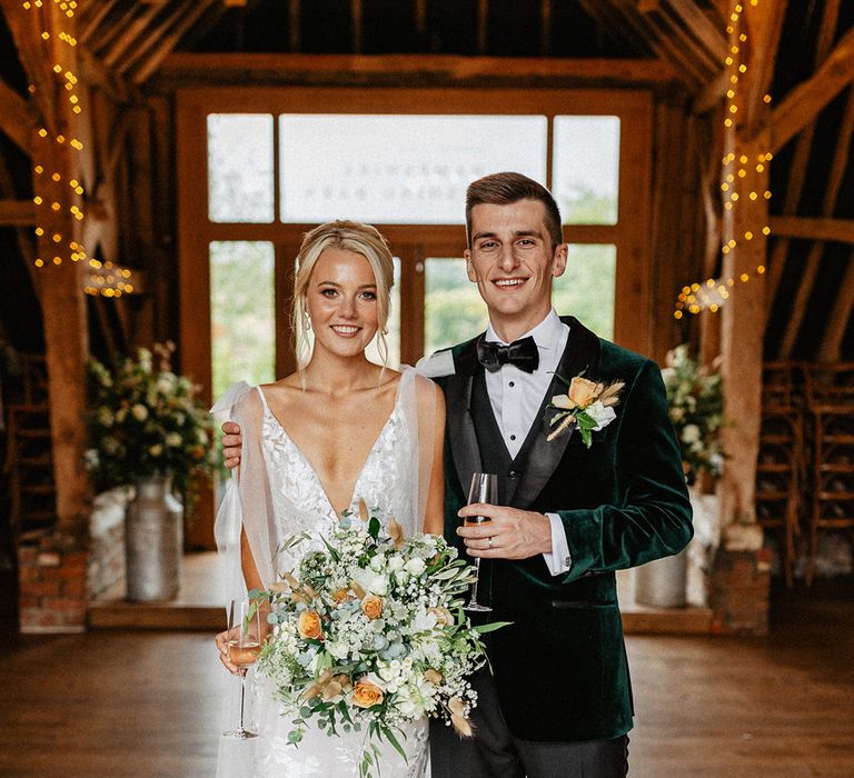 Groom in green velvet tuxedo embracing the bride in a fitted lace bridal gown holding the bridal bouquet 