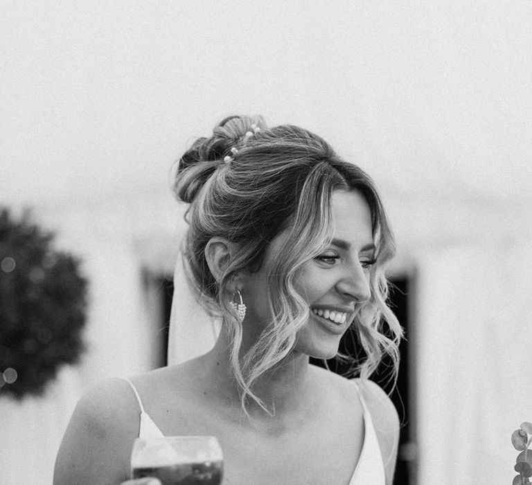 V neck satin wedding dress worn by the bride with thin spaghetti straps holding a glass of alcohol to celebrate her marriage 