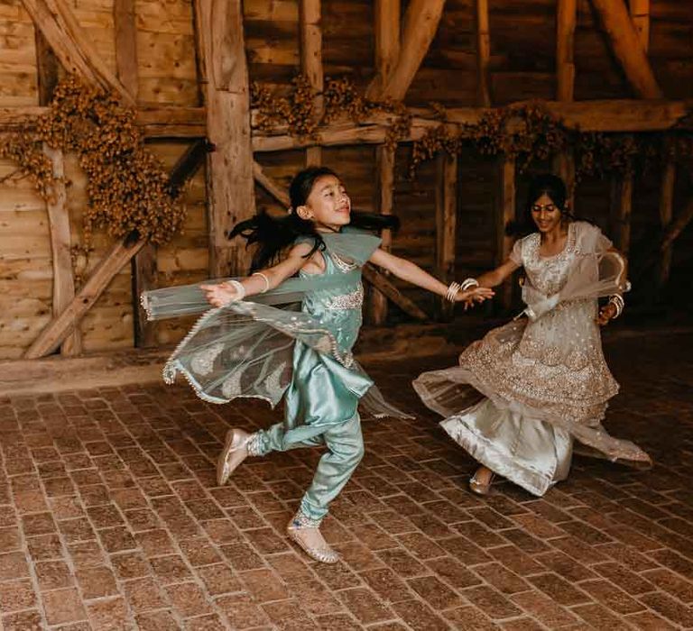 Young wedding guests in teal and gold lehengas dancing at High Billinghurst Farm