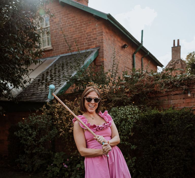 Wedding guest in pink wedding guest outfit waving mallet for game of croquet 