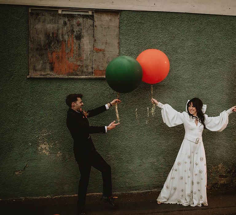 70s theme wedding with the bride and groom posing with huge red and green balloons 