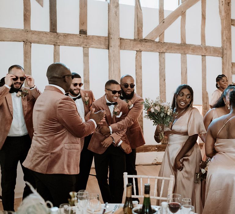 The bridesmaids in pink satin dresses and groomsmen in pink velvet suits all dance together on the dance floor 