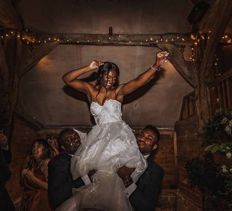 Bride in sweetheart neckline lace wedding dress being lifted up by groomsmen during wedding disco 