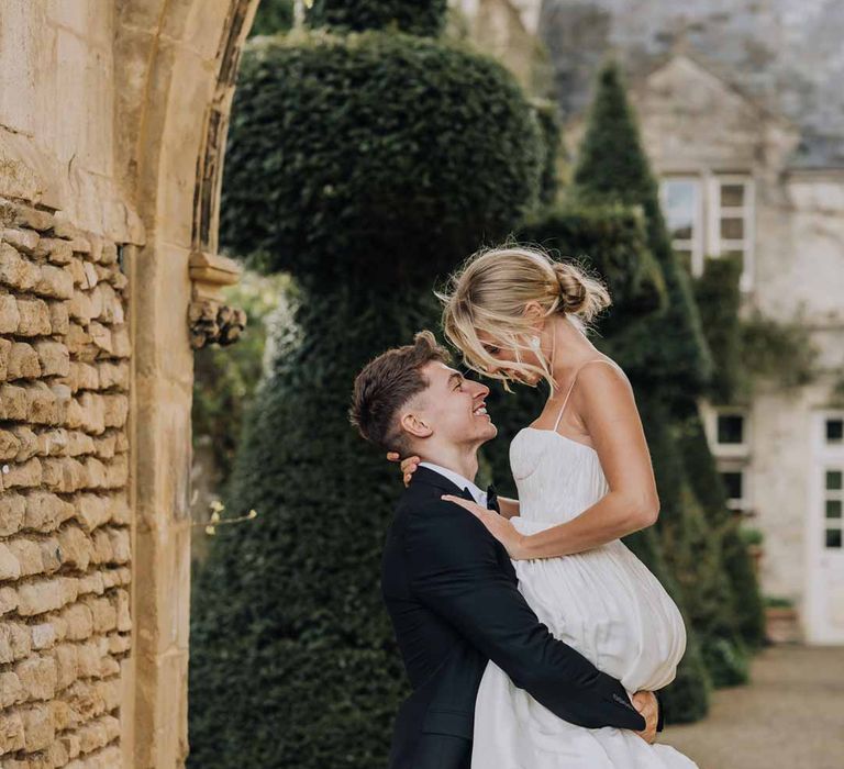 Groom in classic black tuxedo picking up bride in Watters strappy sleeveless princess wedding dress  