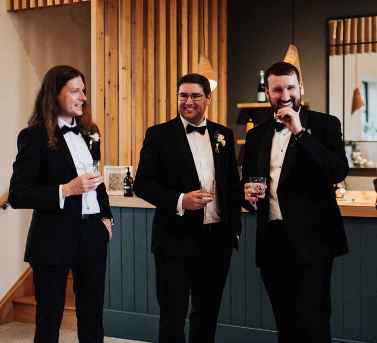 Groomsmen wearing matching classic black three piece grooms tuxedos with white rose boutonnieres and black bowties 