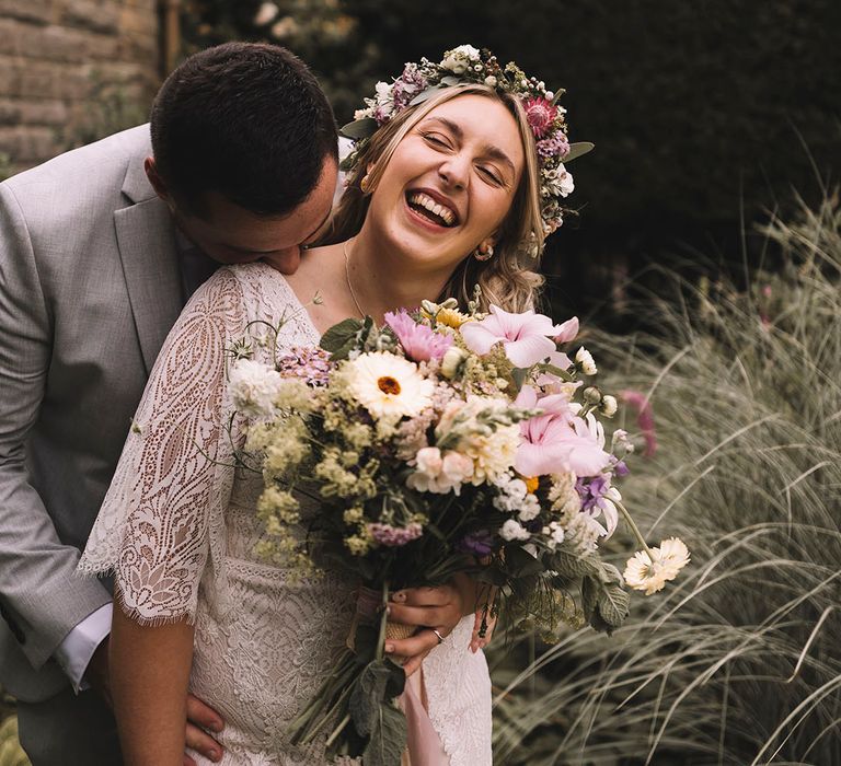 Bride laughing wearing wildflower wedding crown holding pastel bouquet in lace wedding gown 