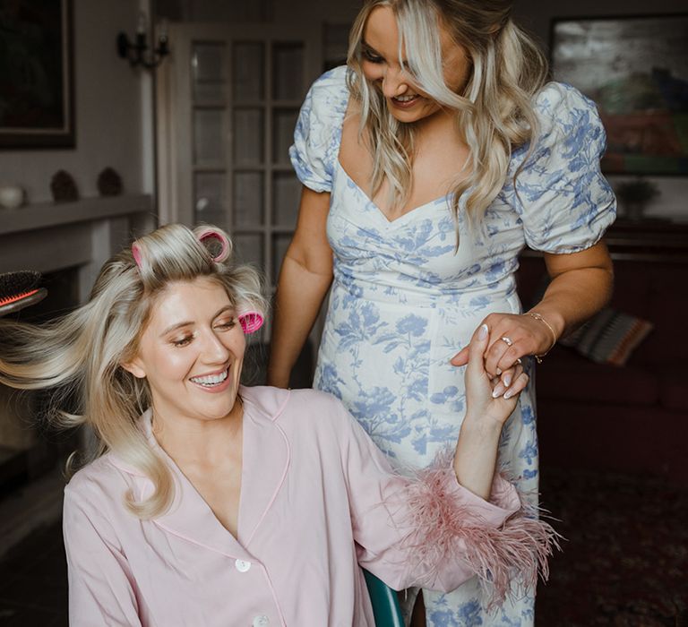 Bride in pink pyjamas with pink feather cuff detail gets her hair done for the wedding day 