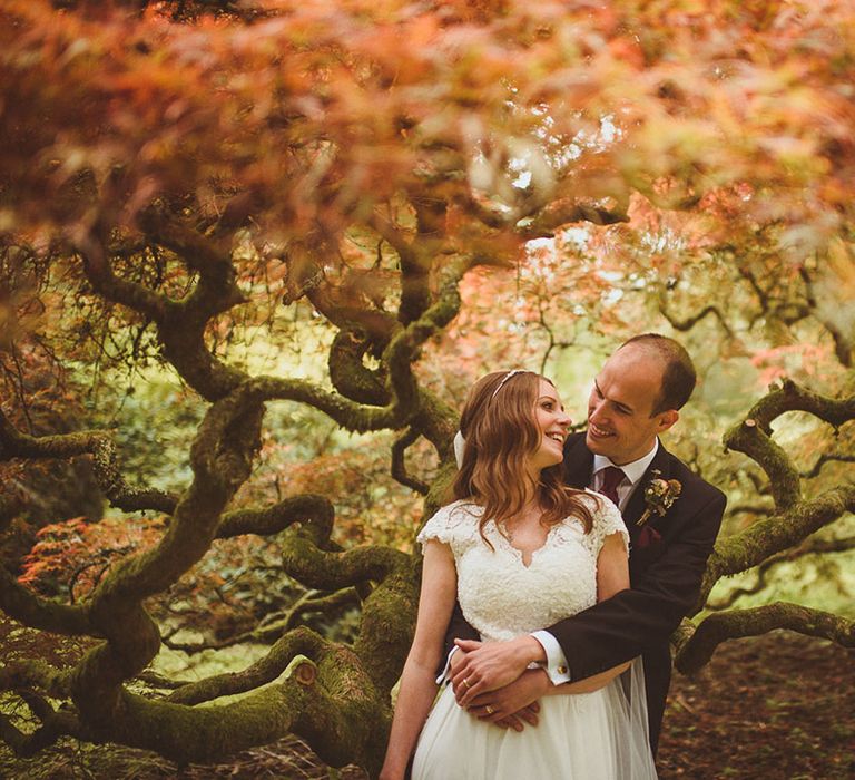 Autumnal theme wedding in October with the groom embracing the bride from behind in the woods at the venue 