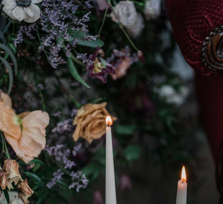 Neutral tapered candles in gold candlesticks surrounded by suspended wildflower and foliage arrangements in large gold vases at Buxted Park