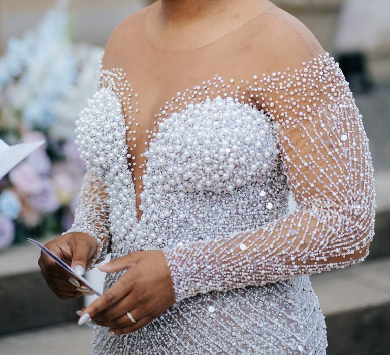 Bride reading her vow renewal wearing illusion v-neck sheer off shoulder long sleeve pearl embellished wedding gown at outdoor ceremony at Syon Park