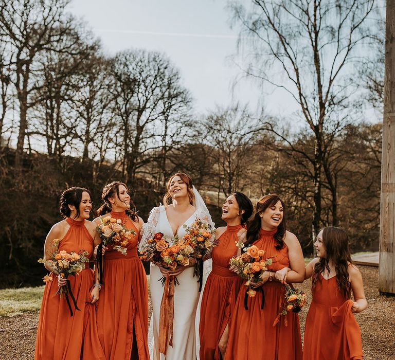 Bridal party wearing matching halter neck orange bridesmaid dresses for autumnal wedding 