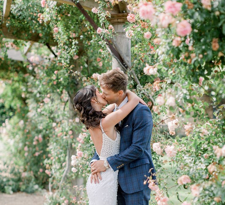 groom in a blue check suit kissing his bride in a fitted appliqué wedding dress