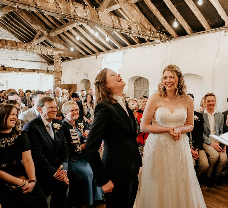 LGBTQIA+ stanford farm wedding with bride in a navy suit laughing at the altar with her bride in a strapless lace wedding dress