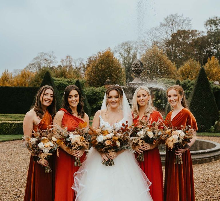 Bridal party wearing orange velvet bridesmaid dresses for autumn themed wedding 