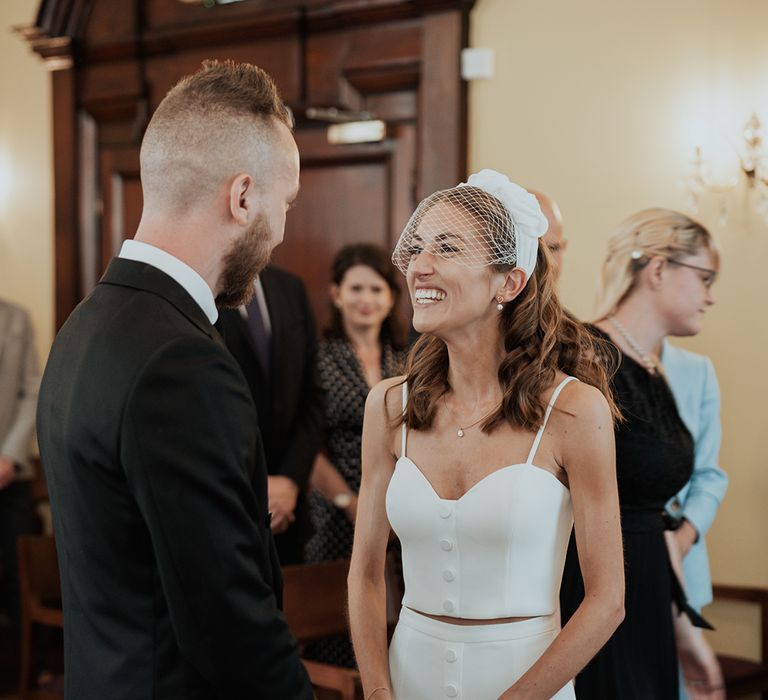 bride in bridal separates and a birdcage veil smiling during the Chelsea registry office wedding ceremony 