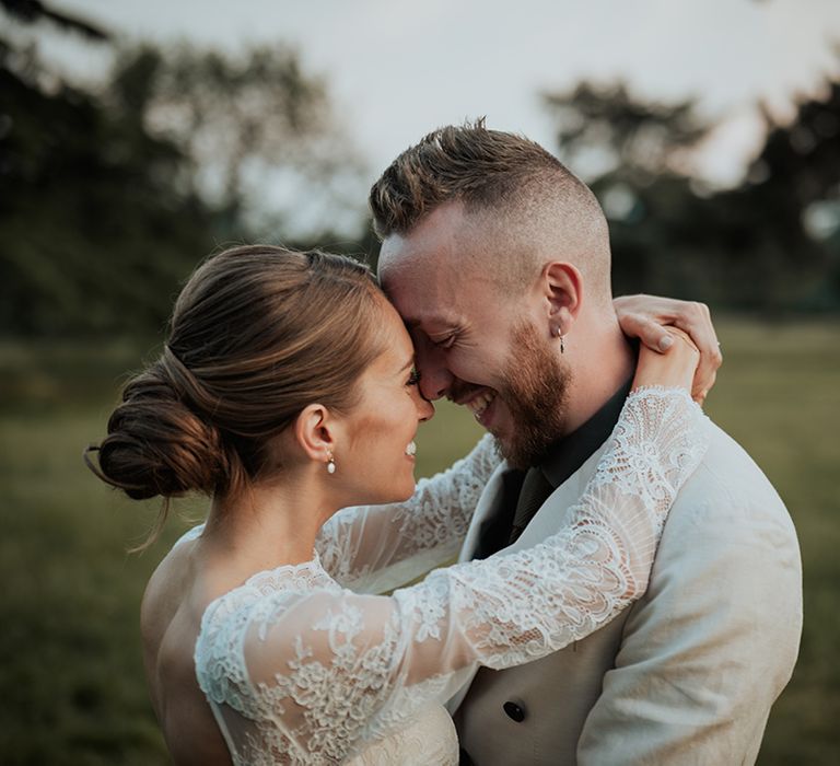 bride with a low bridal bun and lace long sleeve wedding dress embracing her groom in a beige wedding suit