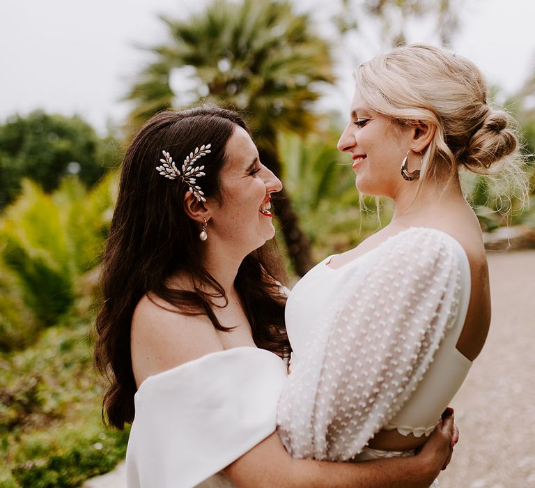 Bride with side swept hair and pearl hair accessory embracing bride in two piece top and skirt 