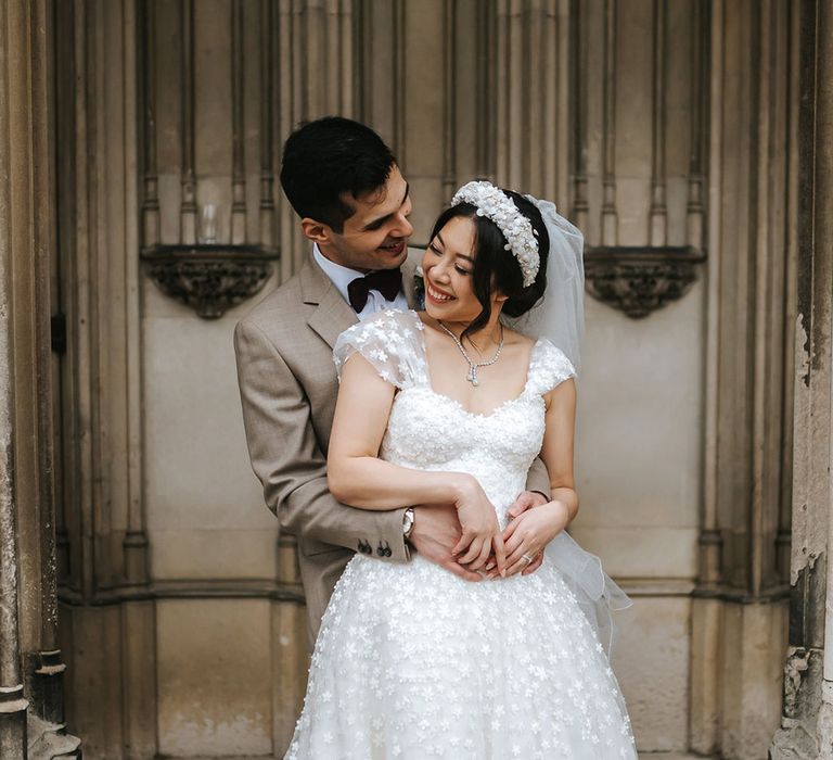 Bride in Sassi Holford wedding dress with statement pearl headband kissing the groom 