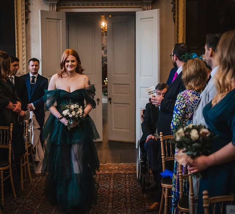 Bridesmaid wearing tulle emerald green bridesmaid dress walking down the aisle 