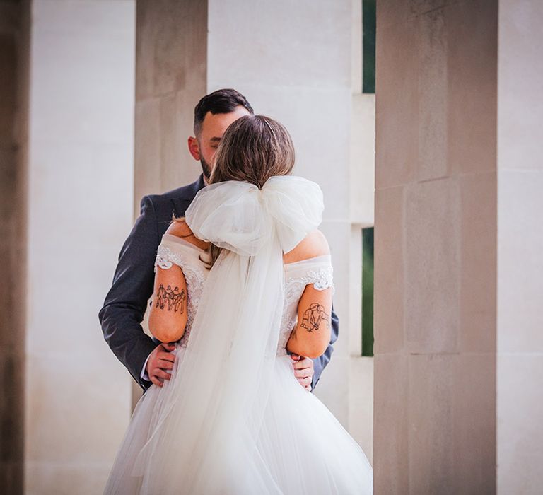 Bride in off the shoulder gown wearing oversized bow wedding veil 