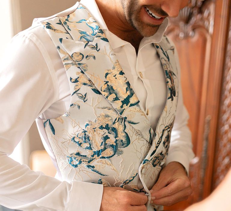 Groom putting on floral waistcoat as he gets ready for the wedding 