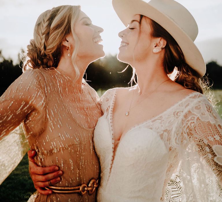 Boho brides with one wearing a sparkly gold reception dress and the other bride wearing a boho lace wedding dress and white hat for golden hour 