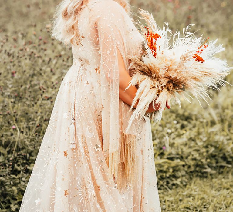 Bride with half up half down hair in gold metallic wedding dress with boho pampas grass and dried flower bouquet 