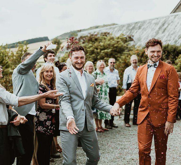 The groom in a grey suit stands with groom in a burnt orange suit for LGBQTI same sex wedding 