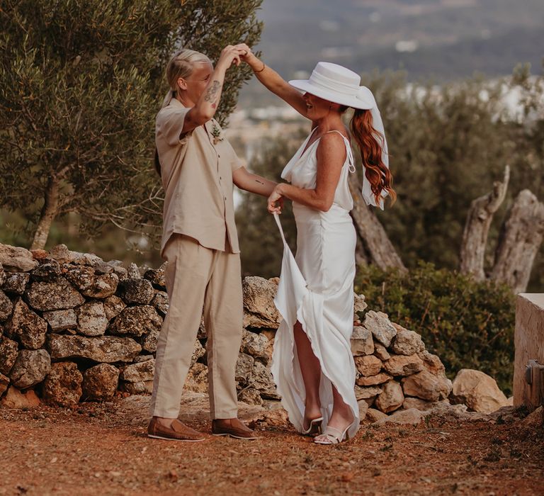 Two brides pose together for their couple portraits with rustic backdrop of Ibiza 