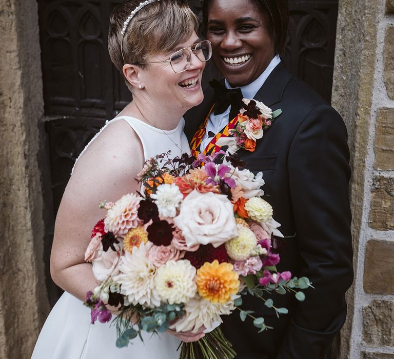 Bride holding colourful autumnal wedding bouquet with the bride in wedding suit at LGBTQI+ wedding 