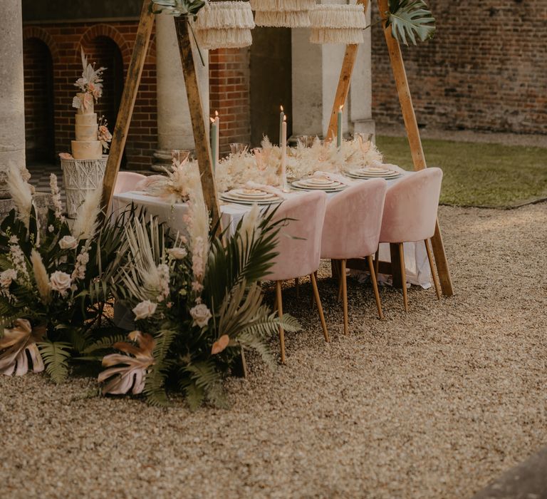 Outdoor wedding reception table with velvet chairs, tropical plants and fabric chandeliers 