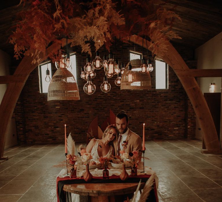 Bride and groom sitting at a cog wheel sweetheart table with light installation