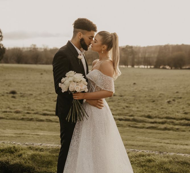 Bride in sparkly wedding dress and groom in tuxedo kissing at Gosfield Hall wedding venue 