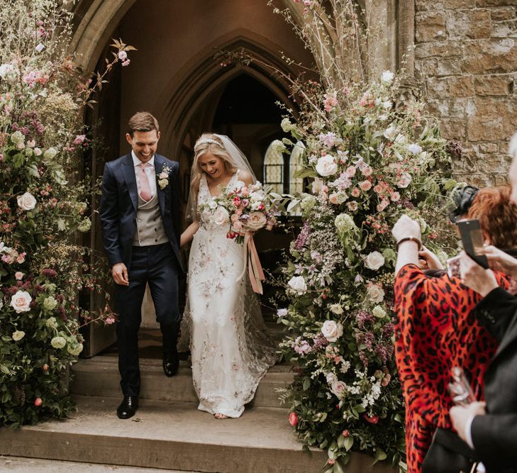 Bride and groom exiting the church with flower arrangements 