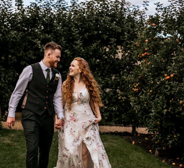 Bride & groom walk through gardens holding hands