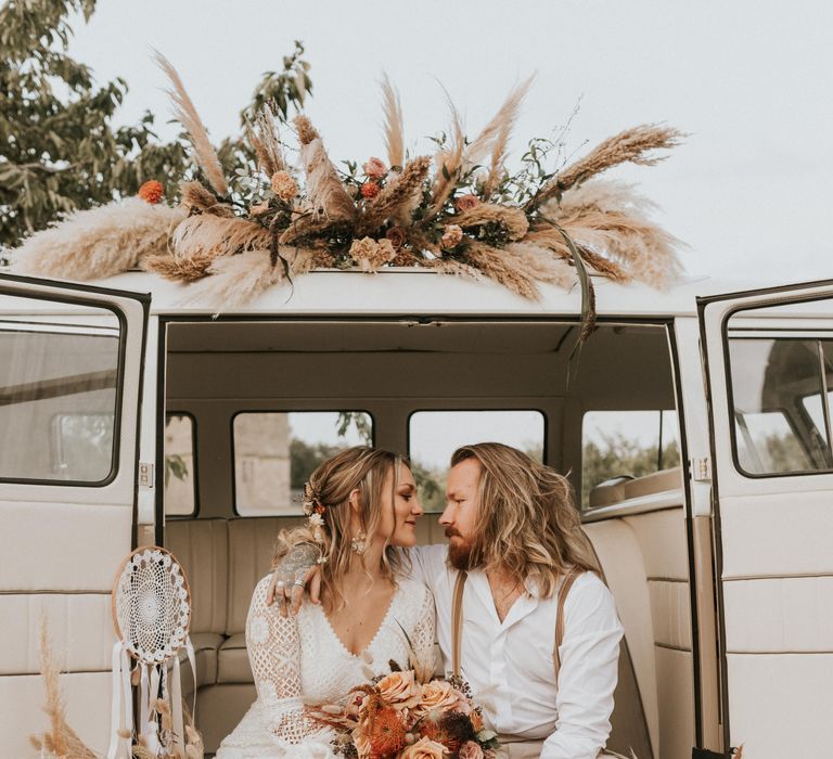 Bride & groom sit outside Camper Van with floral decoration 