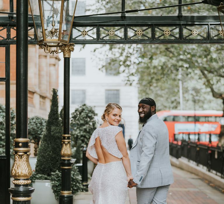 Bride in sparkly bridal separates with gapping back detail and groom in a light grey suit holding hands 