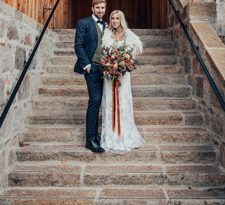 Bride & groom pose together on steps whilst bride wears feathered shawl